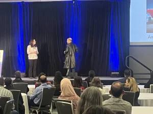 Suzannah Baum at a speaking event with a man in black jacket who walked on the stage in the middle of the Q&A session.